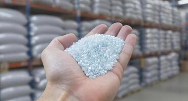 Close up of a hand holding light blue plastic pellets in a factory warehouse photo