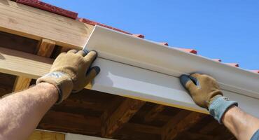 Professional worker installing white plastic soffit panel on building roof structure photo