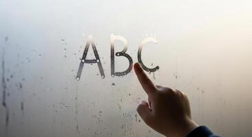 Small child finger tracing ABC letters on a condensation covered window photo