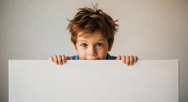 Curious young boy peeking over blank white canvas with copy space photo