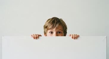 Curious little boy peeking over a blank white canvas with wide eyes photo