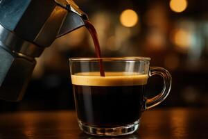 Rich espresso coffee with crema pouring from moka pot into clear glass cup photo