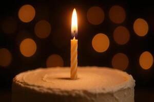 Close up of a single burning birthday candle on a frosted cake with soft warm bokeh lights photo