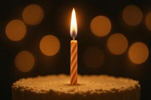 Single birthday candle burning brightly on a cake with warm bokeh lights photo