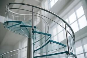 Modern spiral staircase with transparent glass steps and stainless steel handrail in a bright interior photo