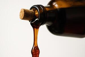 Close up of viscous amber syrup pouring from a rustic glass bottle with a cork photo
