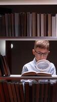 A boy in glasses is looking at a book through a magnifying glass video