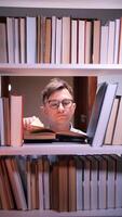 vertical Young man reading a book in a library surrounded by bookshelves video