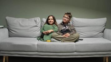 Two children sitting on a couch in front of a green wall video