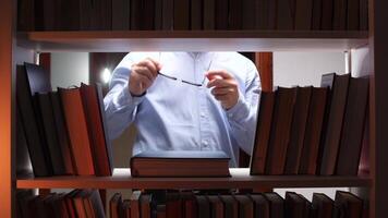 Librarian holding eyeglasses in library at night, surrounded by books video