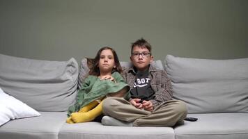 Two children sitting on a couch with a remote control video