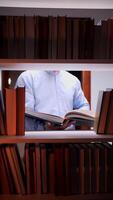 vertical Man reading a book between bookshelves in a library video