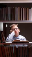 A boy in glasses is sitting on a shelf with books video