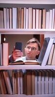 vertical Man reading and using smartphone in a library at night video