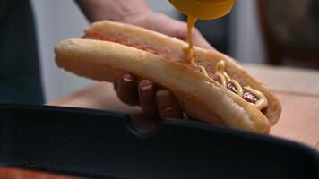 Close-up of a hand adding mustard sauce to a freshly grilled hot dog in a modern kitchen setting video