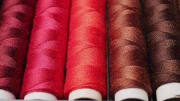 Close-up of vibrant red and brown sewing thread spools perfectly arranged in a neat row on a gray surface video