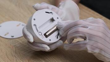 Close-up of hands in gloves inserting battery into smoke detector on wooden surface for home safety maintenance video