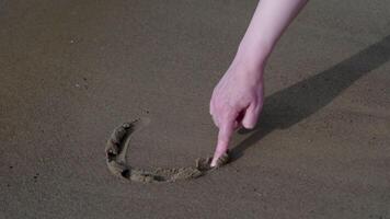 Close-up of a hand drawing a heart shape in soft sand on a peaceful beach shore video