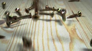 Close-up dynamic view of metal screws falling and scattering on light wooden surface with natural texture video