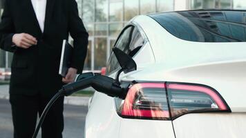 A confident businessman next to his electric car waiting for charging to finish. The concept of clean energy and sustainable development, emphasizing the importance of green technology. video