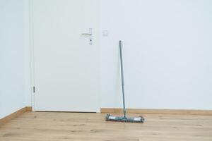 An empty room with a wooden door and a mop lying on the floor photo