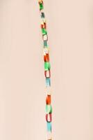 Vertical chain of interlinked colorful paper rings suspended against soft beige background. This vibrant handmade garland , childhood creativity, festive decor, crafting with simple materials photo