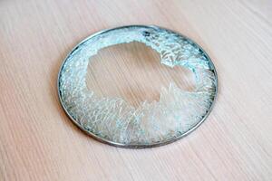 close-up shot of shattered glass circular lid with metal rim from cooking pot, resting on wooden surface, large central break with jagged, splintered edges, suddenness of an accident in kitchen photo