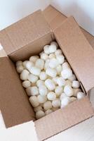 Open cardboard box filled with eco-friendly corn-based packing peanuts on a light wooden surface. Sustainable packaging for safe and conscious shipping, promoting zero-waste photo
