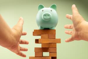 A piggy bank stands on precariously Jenga blocks with hands protecting it, symbolizing fragile financial stability and economic uncertainty, need for caution photo