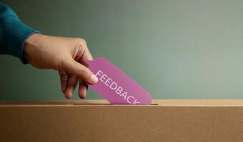 Hand putting feedback card in box symbolizing customer review, survey response, and constructive evaluation photo