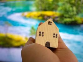 Holding a miniature house model near a scenic river nature close-up tranquil concept of home photo