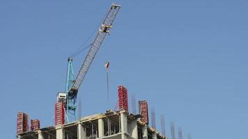 A crane maneuvering materials high above a construction site while workers prepare building structures. The activity shows ongoing site development video
