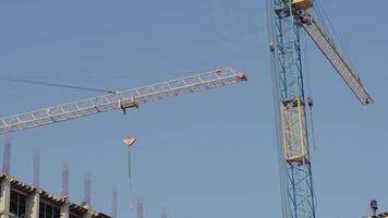 Cranes are actively lifting heavy machinery at a construction site, emphasizing the building process under clear skies video