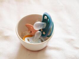 Colorful baby pacifiers a bowl home soft environment close-up parenting concept photo