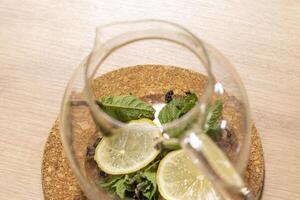 Stylish transparent tea pot with dried tea leaves, mint leaves and lemon slices in it. Beverage photo