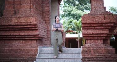 Handheld low angle view shot, Happy young woman in casual clothes walking exploring and enjoying taking photos at an ancient site, Enjoy holiday travel. video