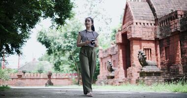 Handheld low angle view shot, Happy young woman is enjoying a quiet stroll, taking photos of old sculptures and ancient brick structures, Enjoy holiday travel. video