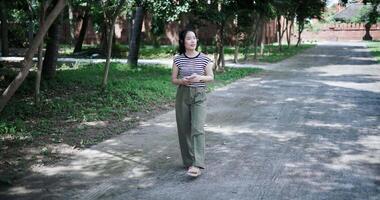 Handheld high angle view shot, Relaxed Asian woman listening to music on wireless headphones over a mobile app while walking leisurely in a quiet place. video