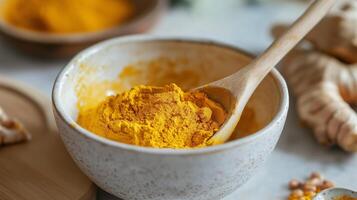 Turmeric powder in a bowl with wooden spoon surrounded by fresh ginger and spices in a cozy kitchen setting photo