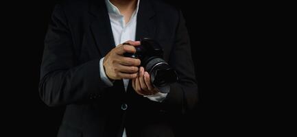 Close-up of a photographer in a suit holding the digital camera while standing on a black background photo
