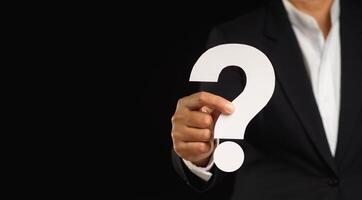 Close-up of a businessman holding a white question mark symbol while standing against a black background photo