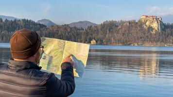 A contemplative Asian man with a map beside tranquil lakeside scenery, embracing Wanderlust Day and Cartography Week explorations photo