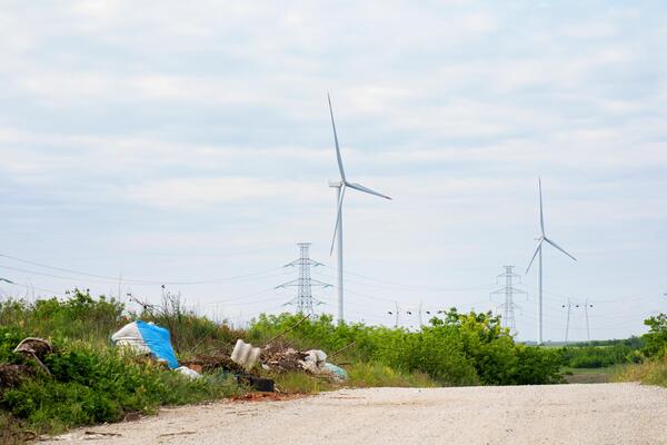 Wind turbines whirl majestically above a rustic path, embracing Earth Days sustainable spirit amidst unexpected roadside debris whispers