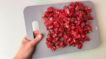 Hand gripping cutting board adorned with vibrant diced beef, ready for carnivorous feasts, reminiscent of South American asados photo