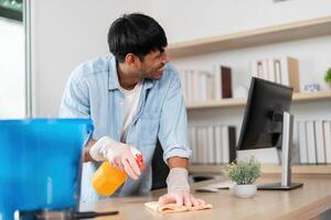 Office Cleaning and Maintenance. Young man using spray cleaner and cloth to tidy workspace. photo