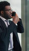 Vertical view angry mad stressed African American business man talking arguing mobile phone call problem discuss in office ethnic rage furious businessman male guy argument quarrel looking in window video