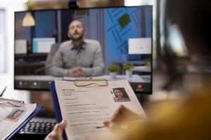 Closeup of cv resume of female job candidate being help by a person during a meeting with remote manager. Selective focus of a curriculum vitae in the hands of an individual attending a call. photo