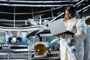 Female astronaut scientist running telemetry software on notebook. Woman researcher wearing cosmonaut gear in spaceship doing research, managing systems and checking diagnostics using laptop photo