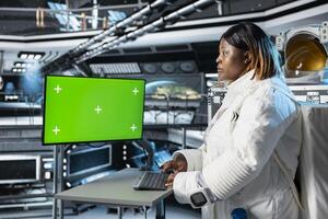Astronaut reviewing spacecraft analytics on green screen monitor to ensure safe operation during long distance space travel. Woman in orbit station uses mockup display during cosmic journey photo