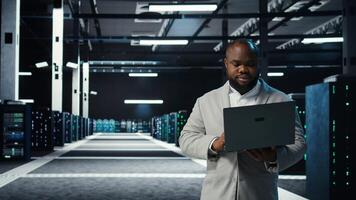 Data center engineer coding on laptop, doing software updates for mainframes. Server farm IT professional typing on notebook keyboard, optimizing infrastructure, camera A photo
